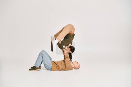 Foto de Joven morena mujer en traje casual equilibrio en las manos de un hombre fuerte, pareja de acróbatas en el estudio - Imagen libre de derechos
