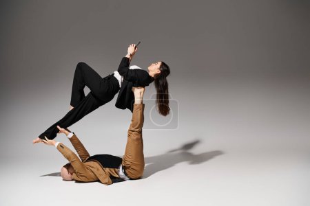 Woman in business wear with smartphone balancing on feet and hands of man, couple of acrobats