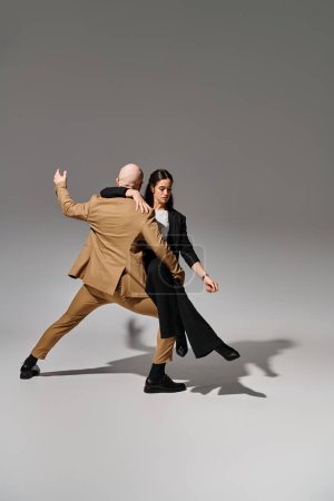 Geschäftsleute in Anzügen führen im Studio vor grauem Hintergrund einen dynamischen Tanzschritt vor, Akrobaten