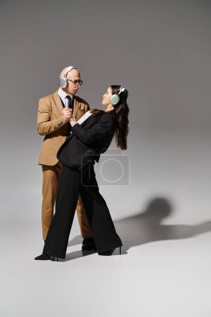 Téléchargez les photos : Acrobates en tenue formelle dans des écouteurs sans fil tenant la main et dansant dans un style de pause de bureau - en image libre de droit