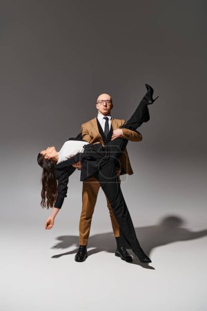 Elegant business couple in a dramatic dance lift in neutral studio setting on grey background
