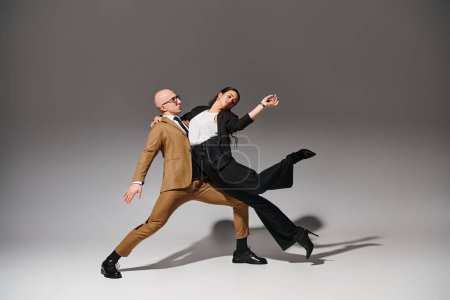 Business couple in stylish suits in creative acrobatic pose, man supporting woman in studio