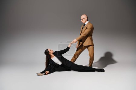 female acrobat in elegant corporate suits executing a split and holding hands with man in studio