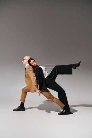 Tanzpartner in koordiniertem Schritt, Frau im Anzug stützt sich auf den Rücken des Mannes in Businesskleidung auf grau