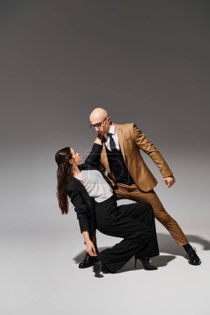 brünette junge Frau in Anzug und High Heels, die mit ihrem Partner vor grauem Hintergrund tanzt