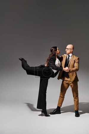 flexible junge Frau in Anzug und High Heels, die mit ihrem Partner vor grauem Hintergrund tanzt