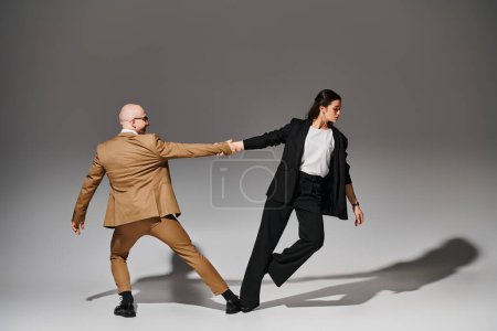 Tanzpartner in formeller Kleidung halten Händchen während des Auftritts im Studio mit grauem Hintergrund