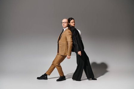 Junges Künstlerpaar in Businesskleidung führt im Studio vor grauem Hintergrund einen Spiegeltanz auf