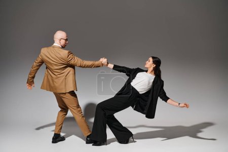 pareja de baile en trajes tomados de la mano durante la actuación en estudio con fondo gris, coreografía