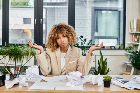 Foto de Confusa mujer de negocios afroamericana rizada en su escritorio con papeles arrugados, estrés en el trabajo - Imagen libre de derechos