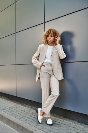 curly african american businesswoman in formal wear posing near office building, young leader