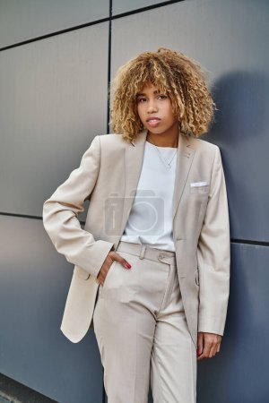 Photo for Curly african american businesswoman in suit posing with hand in pocket near office building - Royalty Free Image