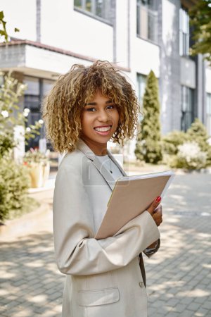 happy african american entrepreneur in braces standing with folder near office building on sunny day magic mug #693353532