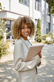 happy african american entrepreneur in braces standing with folder near office building on sunny day Stickers #693353532
