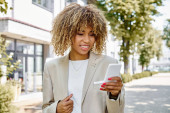 happy african american businesswoman in braces walking with smartphone near office building magic mug #693353628