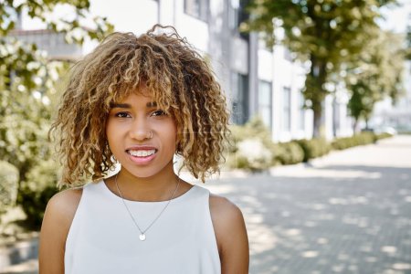 portrait of happy young african american woman with curls posing in summery warm day, street style