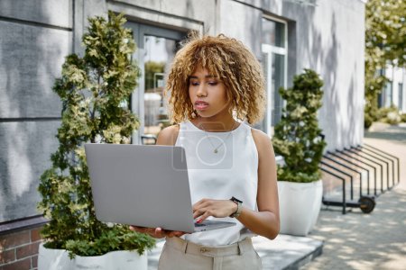Photo for Curly african american woman with braces standing with her laptop near building in warm summer day - Royalty Free Image
