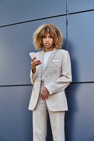 Photo for Young and pierced african american businesswoman with curly hair holding her smartphone outdoors - Royalty Free Image