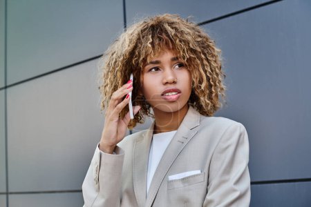 chère et jeune femme d'affaires afro-américaine aux cheveux bouclés parlant sur smartphone à l'extérieur