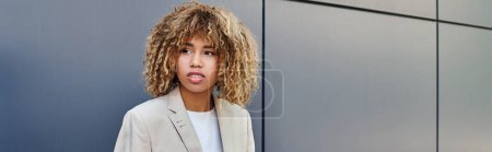 Stylish professional banner, young and curly african american woman sitting by grey office wall