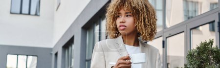 curly african american businesswoman standing with cup of coffee near office building, banner