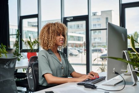 positif jeune gestionnaire afro-américain travaillant au bureau en face de moniteur d'ordinateur dans le bureau