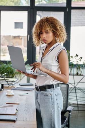 curly african american businesswoman in casual attire working on laptop in a modern office