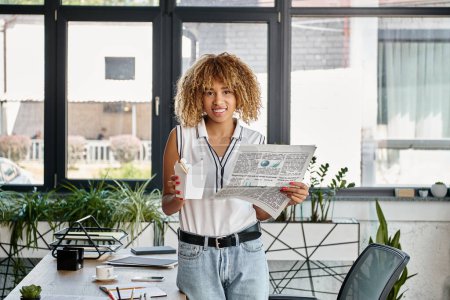 happy african american woman holding asian takeaway meal in carton box and newspaper in office