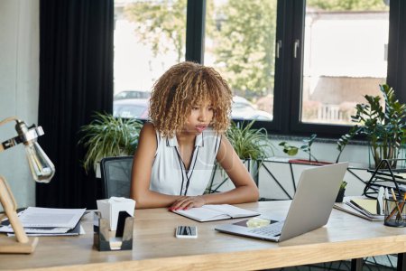 Afrikanisch-amerikanische Geschäftsfrau schaut während eines Videotelefonats im modernen Büro auf den Laptop, Arbeitstag