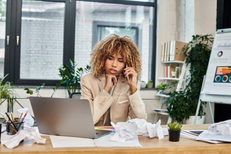 Abrumada mujer de negocios afroamericana multitarea cerca de la computadora portátil y el caos papeleo