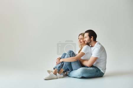 A man and a woman sit closely on the ground, looking away with an aura of love and passion.