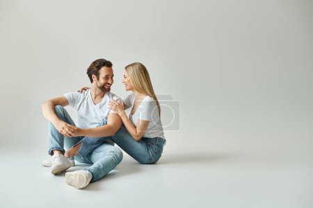 glückliches Paar, in eine intime Umarmung gehüllt, eng am Boden sitzend in einem romantischen Moment.