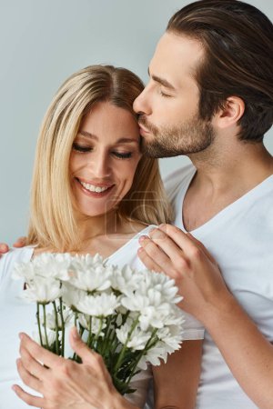 Téléchargez les photos : Un homme embrasse passionnément une femme tout en tenant un bouquet de fleurs, mettant en valeur un lien romantique florissant entre eux. - en image libre de droit