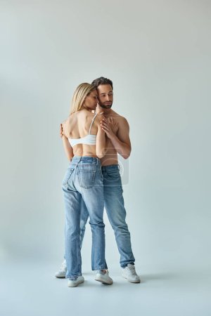 A man and a woman wearing jeans embrace each other in a romantic and intimate moment.