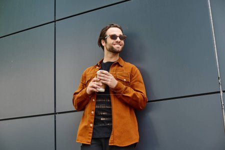 A man leaning against a wall, holding a cup of coffee.
