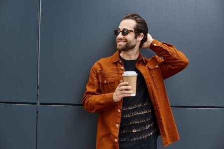 A stylish man in an orange jacket savoring a cup of coffee with a smile on his face.
