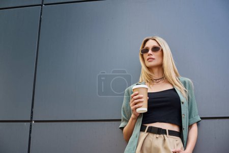 Une femme élégante en haut noir et pantalon bronzé profite d'une tasse de café.
