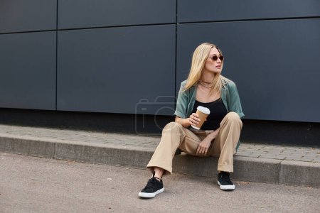 Une femme assise sur le trottoir, tenant une tasse de café.