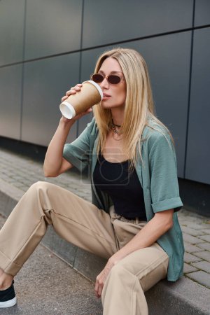 Eine Frau sitzt auf dem Boden und trinkt anmutig aus einer Kaffeetasse in einer ruhigen Umgebung im Freien.