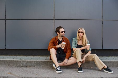 Photo for Couple engaged in a romantic moment, sitting on the curb with coffee - Royalty Free Image