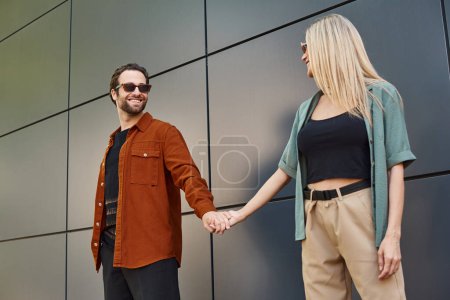Téléchargez les photos : Un couple sexy tenant la main devant un mur, affichant romance et connexion. - en image libre de droit
