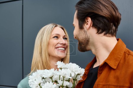Ein Mann steht neben einer Frau und überreicht ihr in einer romantischen Geste einen Strauß weißer Blumen.