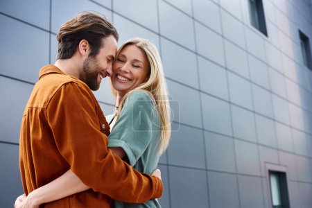 Un momento sensual entre un hombre y una mujer, envueltos uno en los brazos del otro frente a un edificio llamativo.