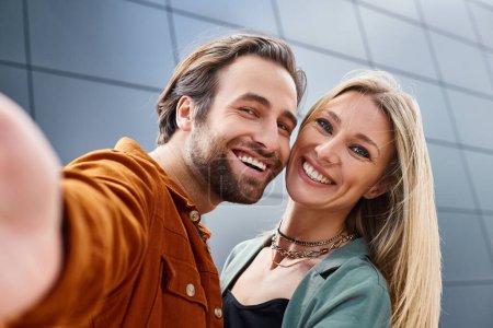 Ein stilvoller Mann und eine stilvolle Frau posieren zusammen und machen ein Selfie vor einem modernen Gebäude.