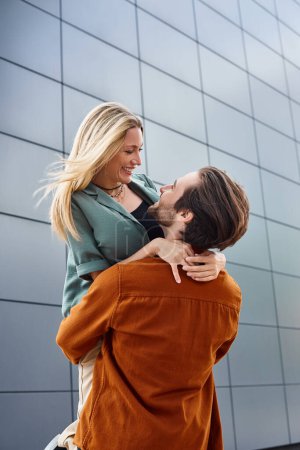 Un hombre sosteniendo a una mujer cariñosamente frente a un edificio urbano llamativo, exudando romance e intimidad en el paisaje urbano.