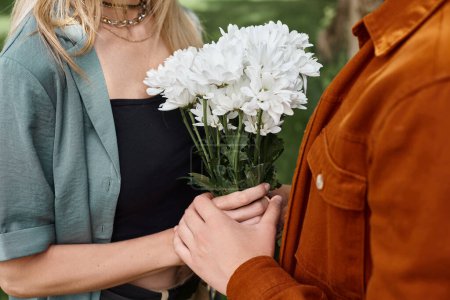 A man holds a bouquet of white flowers next to a woman, showcasing a romantic gesture between a sexy couple.