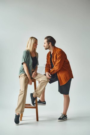 A stylish couple sitting intimately on a stool, exuding romance and allure in their elegant poses.