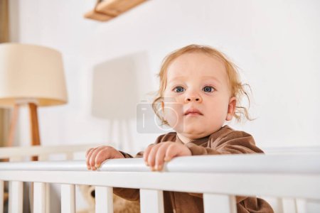 sweet toddler child standing and looking away in crib in nursery room at home, happy childhood