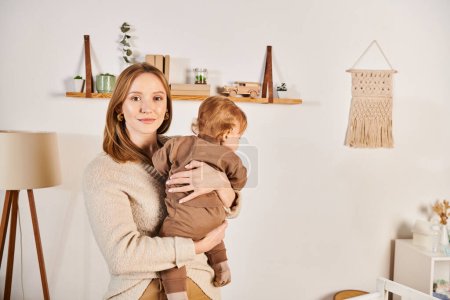 Photo for Happy young woman holding and embracing little toddler son in nursery room, blissful motherhood - Royalty Free Image
