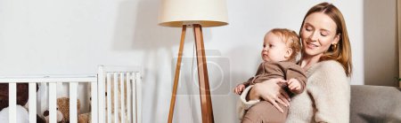 alegre madre con hijo pequeño sentado en sillón cerca de la cuna en la habitación del vivero, pancarta horizontal